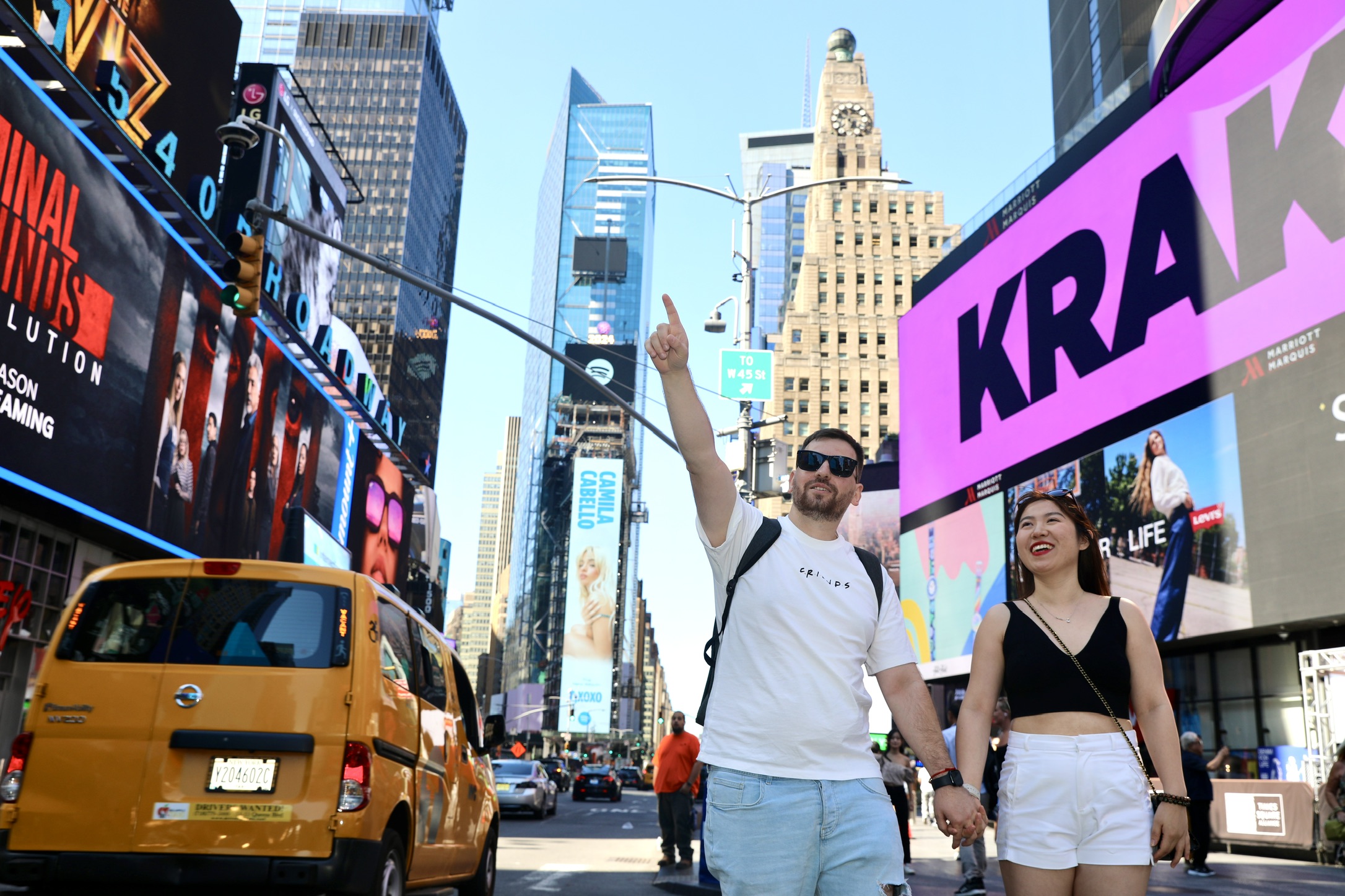 Male pointing out holding hands with an Asian female surrounded by buildings and billboards.