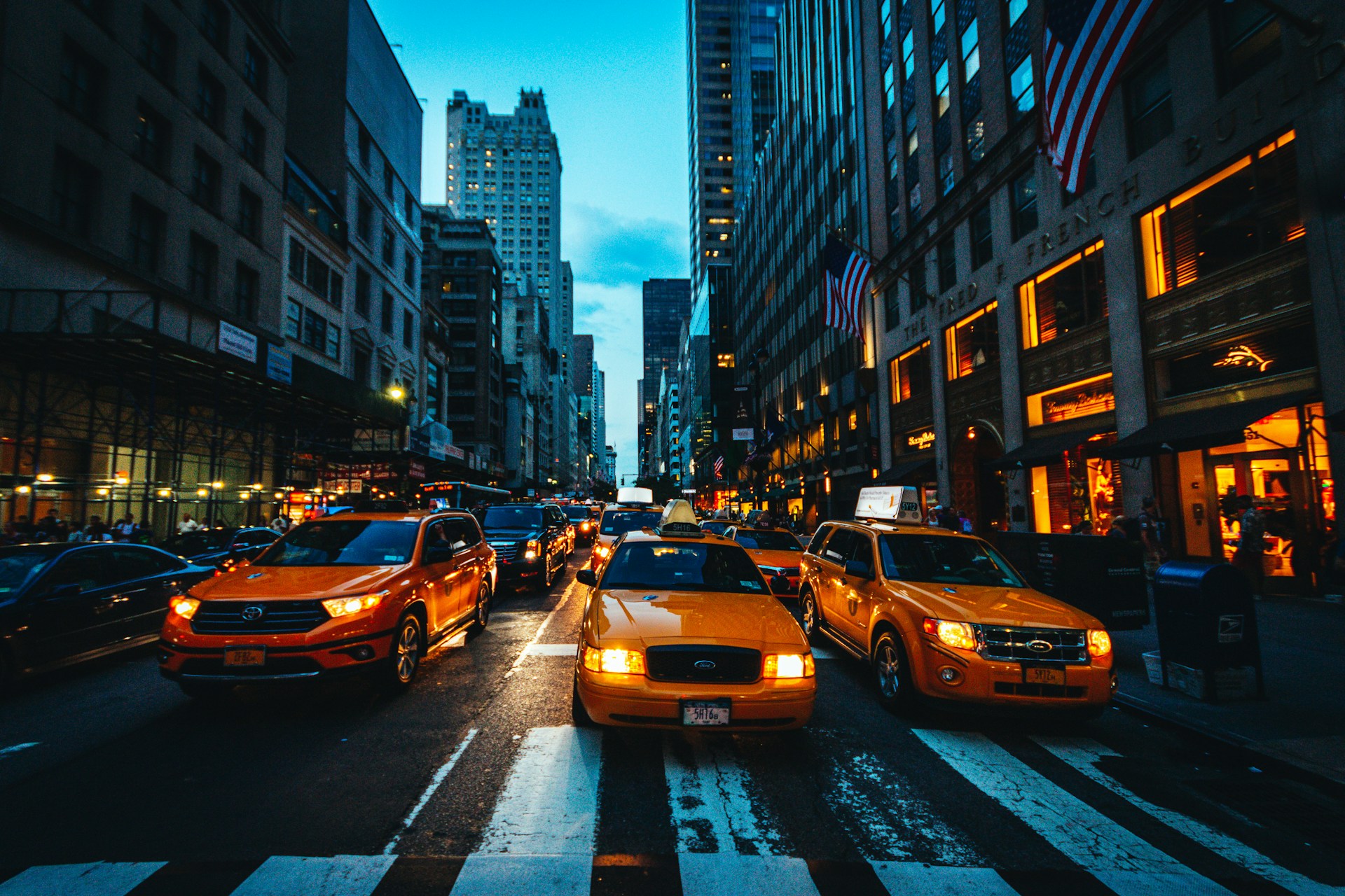 New York City street at dusk with yellow taxis, traffic, and illuminated skyscrapers.